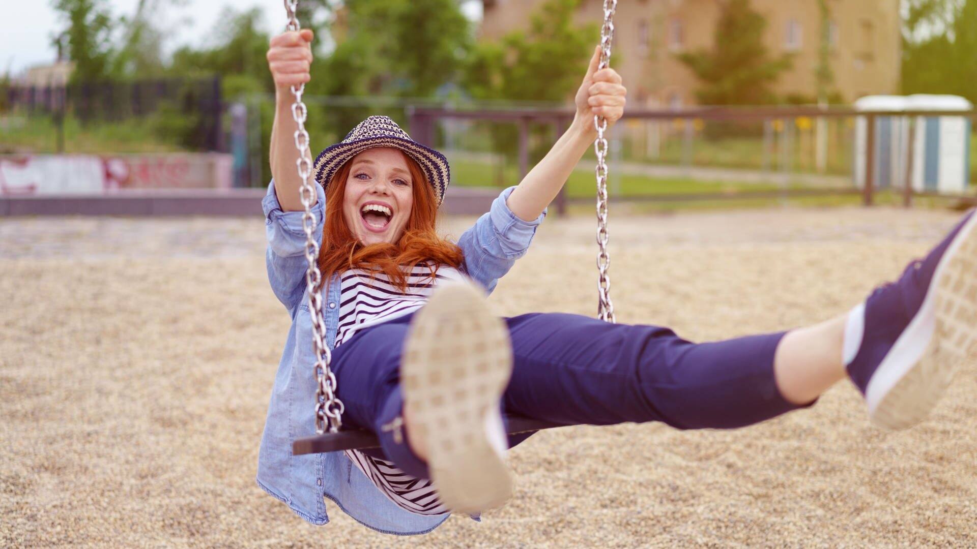 Junge Frau mit Hut schaukelt auf einer Schaukel, sie lacht und freut sich wie ein kleines Kind (Foto: Adobe Stock/contrastwerkstatt )