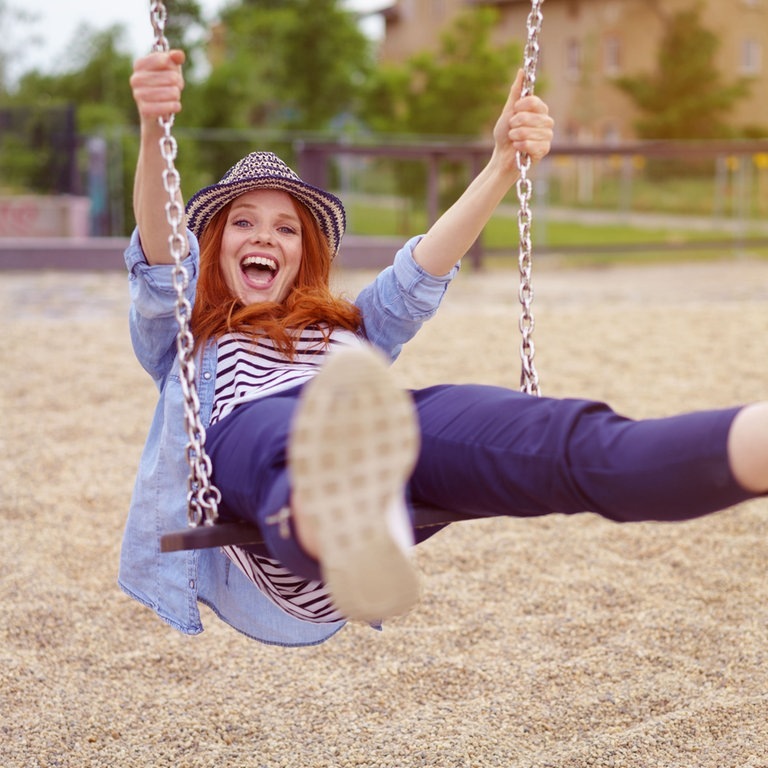 Junge Frau mit Hut schaukelt auf einer Schaukel, sie lacht und freut sich wie ein kleines Kind (Foto: Adobe Stock/contrastwerkstatt )