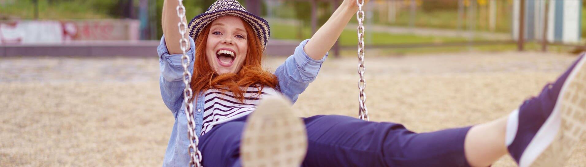 Junge Frau mit Hut schaukelt auf einer Schaukel, sie lacht und freut sich wie ein kleines Kind (Foto: Adobe Stock/contrastwerkstatt )