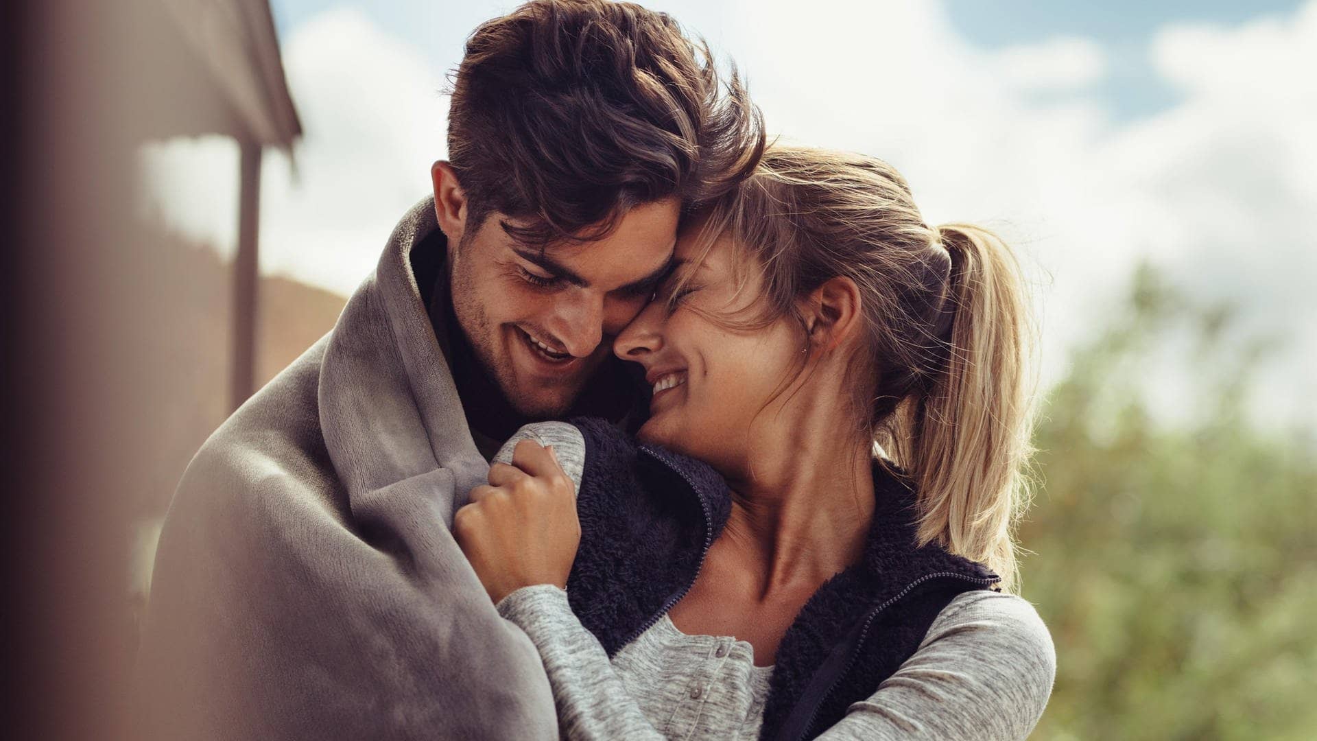 Junges Paar kuschelt verliebt in einer Decke und lächelt sich gegenseitig an (Foto: Adobe Stock/Jacob Lund )