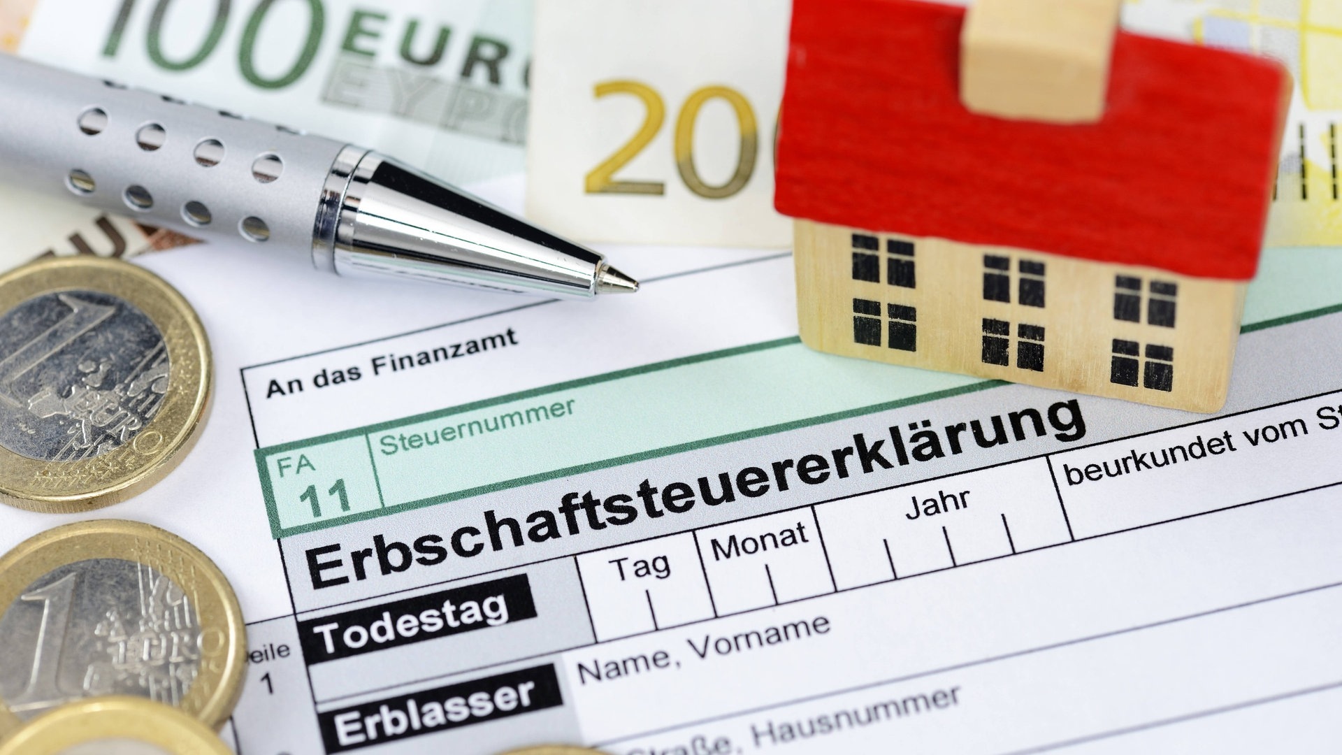 Ein Symbolbild zum Thema Erbe und Erbschaftssetuer. Zu sehen ist ein Formular zur Erbschaftssteuer mit einem Spielzeughaus darauf. (Foto: IMAGO, IMAGO / Christian Ohde)