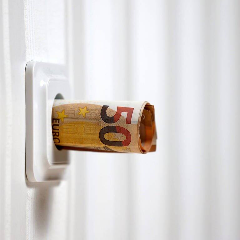 Symbolbild für die Energiekrise: Zusammengerollte Geldscheine ragen aus einer Steckdose.  (Foto: IMAGO, IMAGO / Panama Pictures)