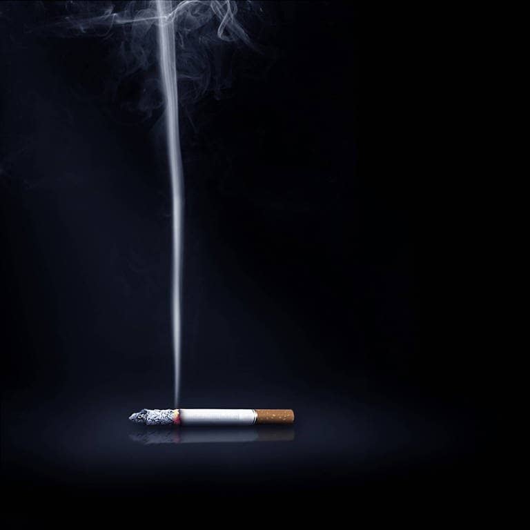 Eine qualmende Zigarette vor schwarzem Hintergrund (Foto: IMAGO, IMAGO / Design Pics)