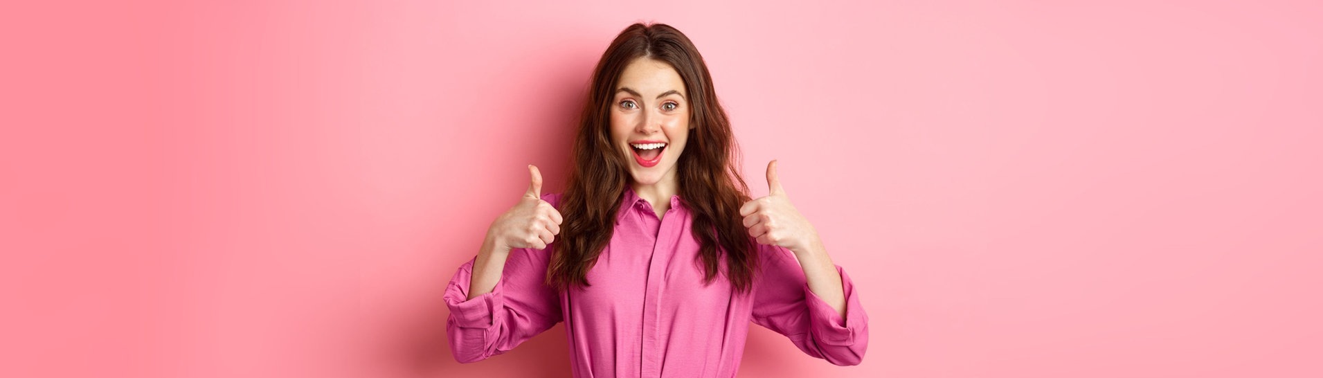 Junge Frau vor pinkfarbenem Hintergrund und mit pinkfarbener Bluse lacht und zeigt mit beiden Daumen in die Luft (Foto: Adobe Stock, Adobe Stock/Mix and Match Studio)