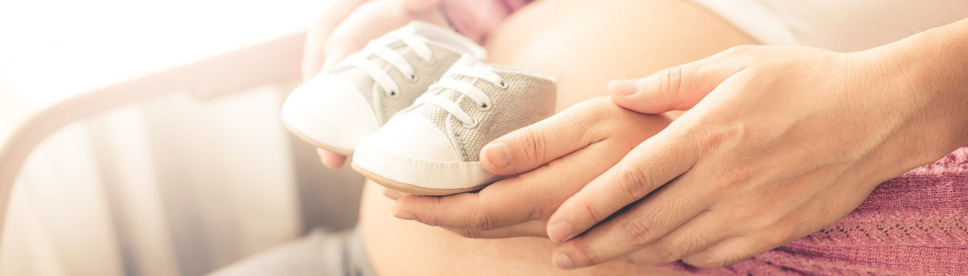 Eine Frau mit Babybauch, die zusammen mit ihrem Partner kleine Babyschühchen darauf hält. (Foto: IMAGO, IMAGO / ingimage)