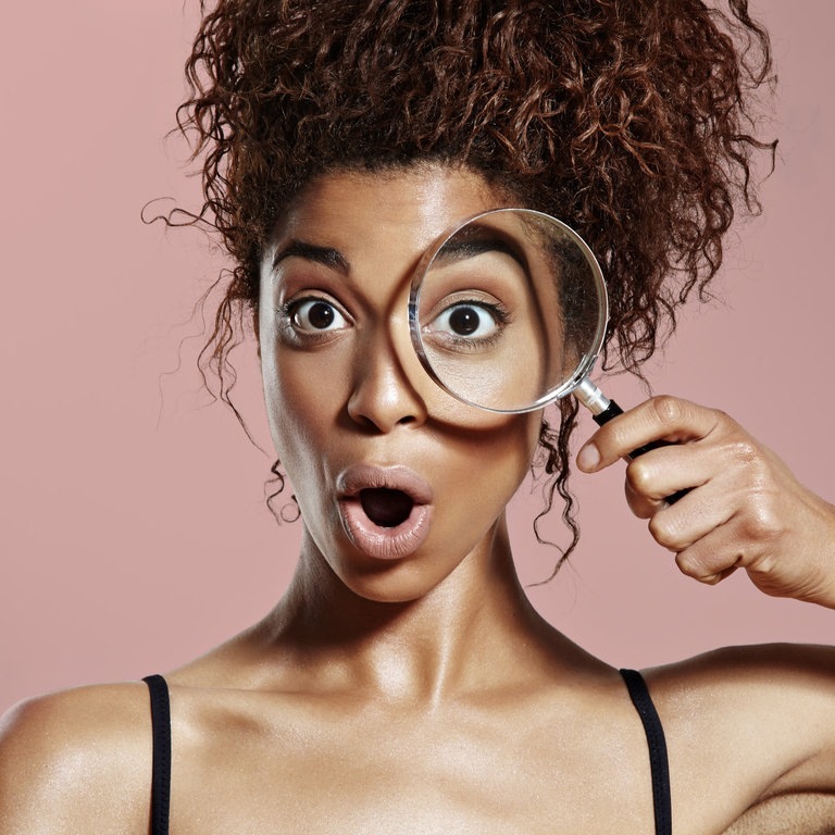 Überraschte Frau schaut durch eine Lupe. (Foto: Adobe Stock, Anastasia)