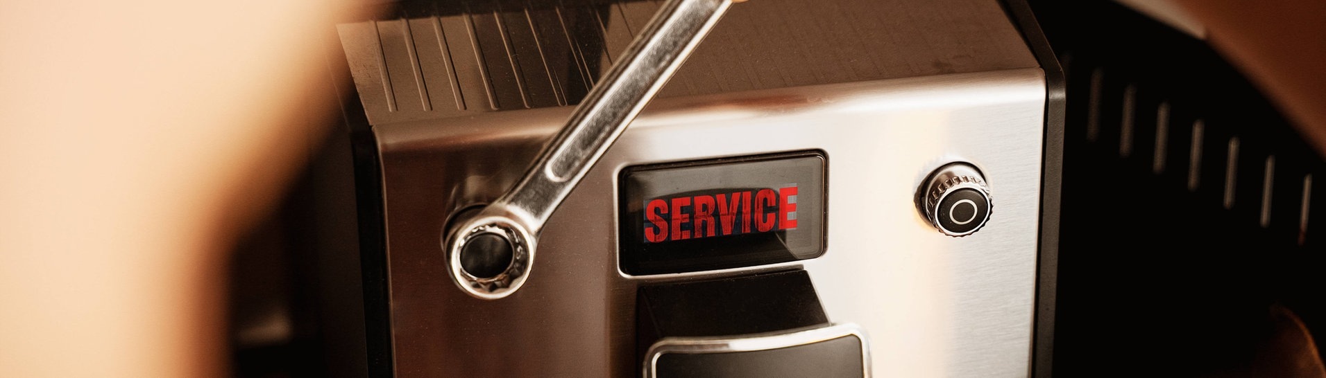 Mann führt den Service mit dem Schraubenschlüssel an der Kaffeemaschine in der Küche durch (Foto: IMAGO, Bihlmayerfotografie)