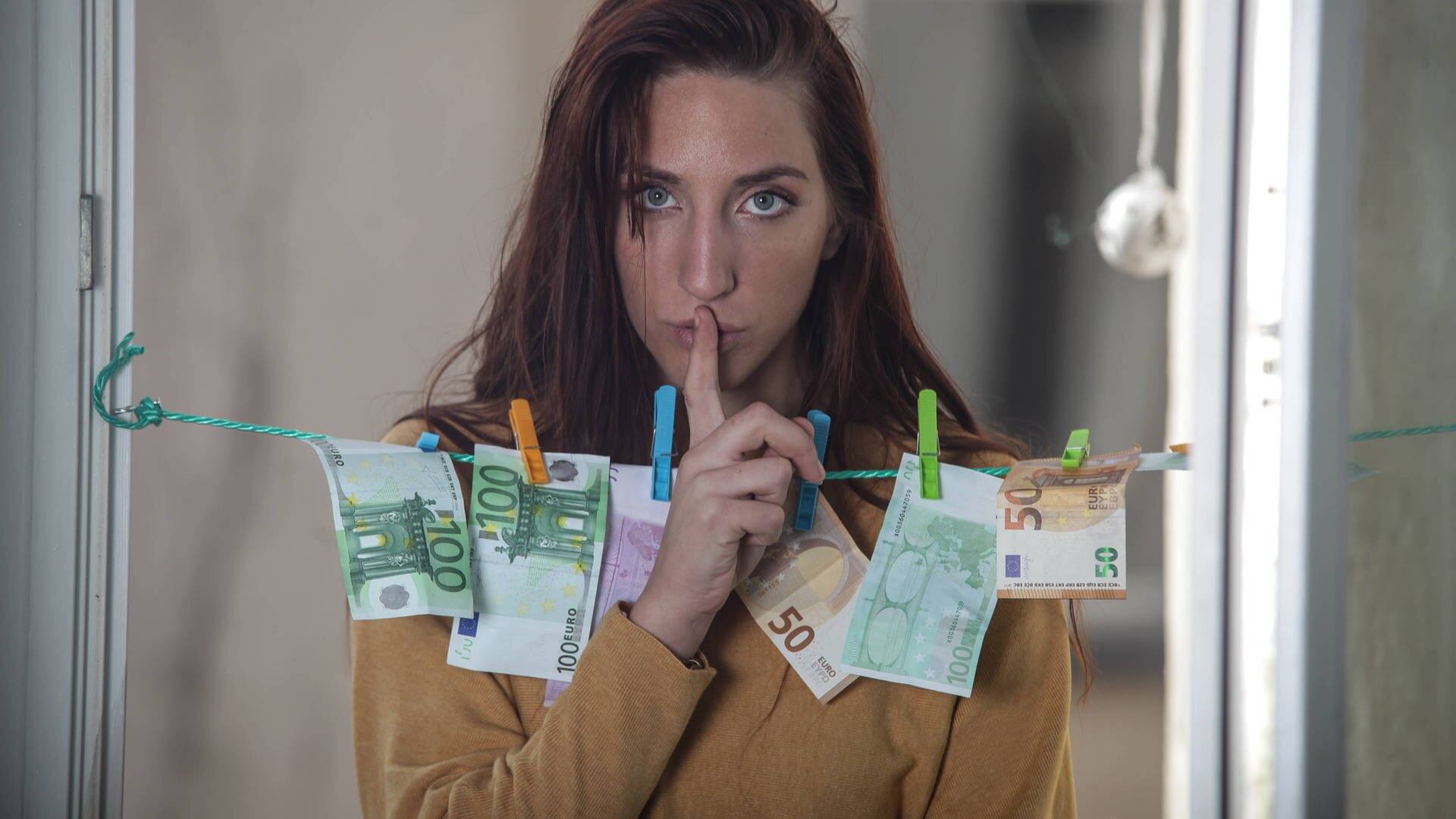 Frau hat Geld auf der Wäscheleine hängen und macht mit dem Finger ein Psst-Zeichen (Foto: IMAGO, Rolf Kremming)