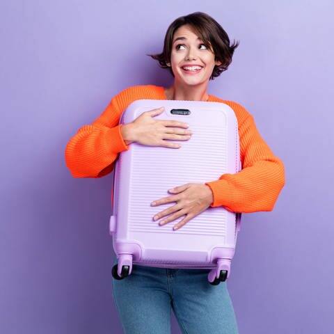Frau hält lilanen Koffer (Foto: Adobe Stock, deagreez)