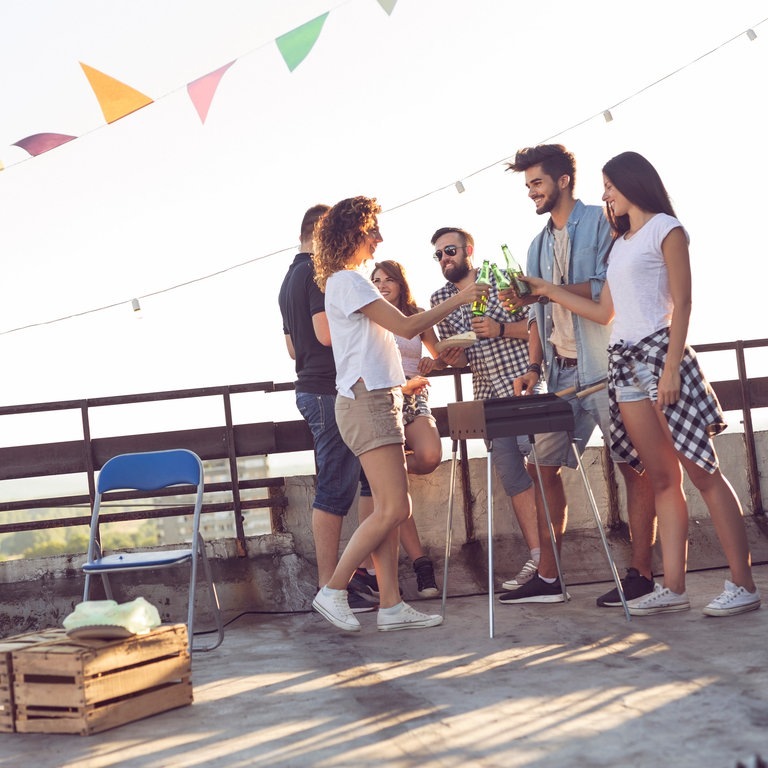 Junge Menschen grillen auf dem Balkon bei abendlicher Sonneneinstrahlung (Foto: Adobe Stock, Impact Photography)