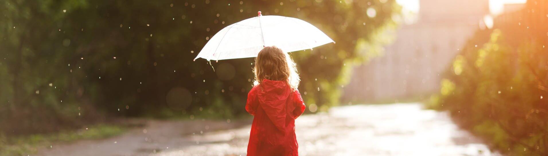 Ein Kind läuft mit Schirm und Gummistiefeln durch den Regen. (Foto: Adobe Stock, ulza)