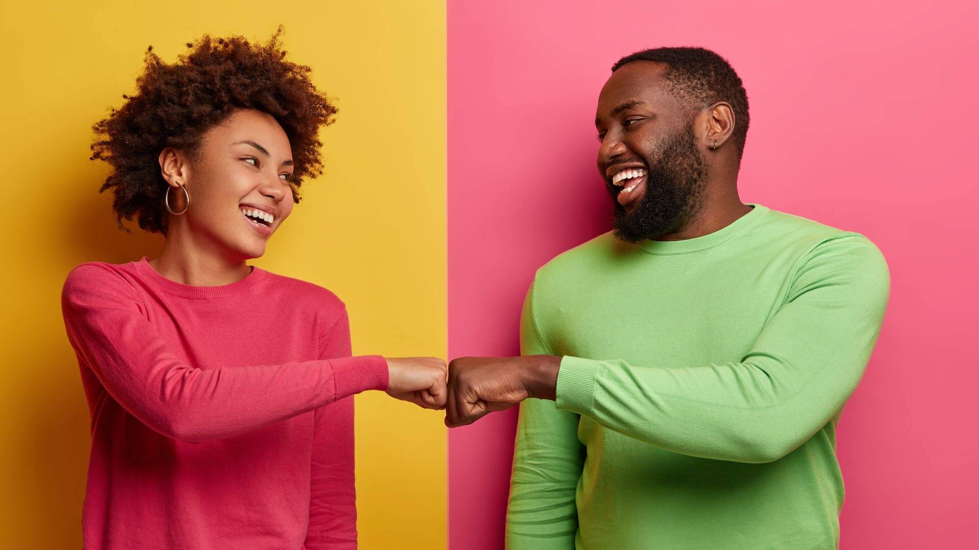 Junges Paar steht lachend vor einer durch zwei Farben getrennten Wand. Sie schlagen sie ab und sehen glücklich aus mit der Beziehung. (Foto: Adobe Stock, Wayhome Studio)
