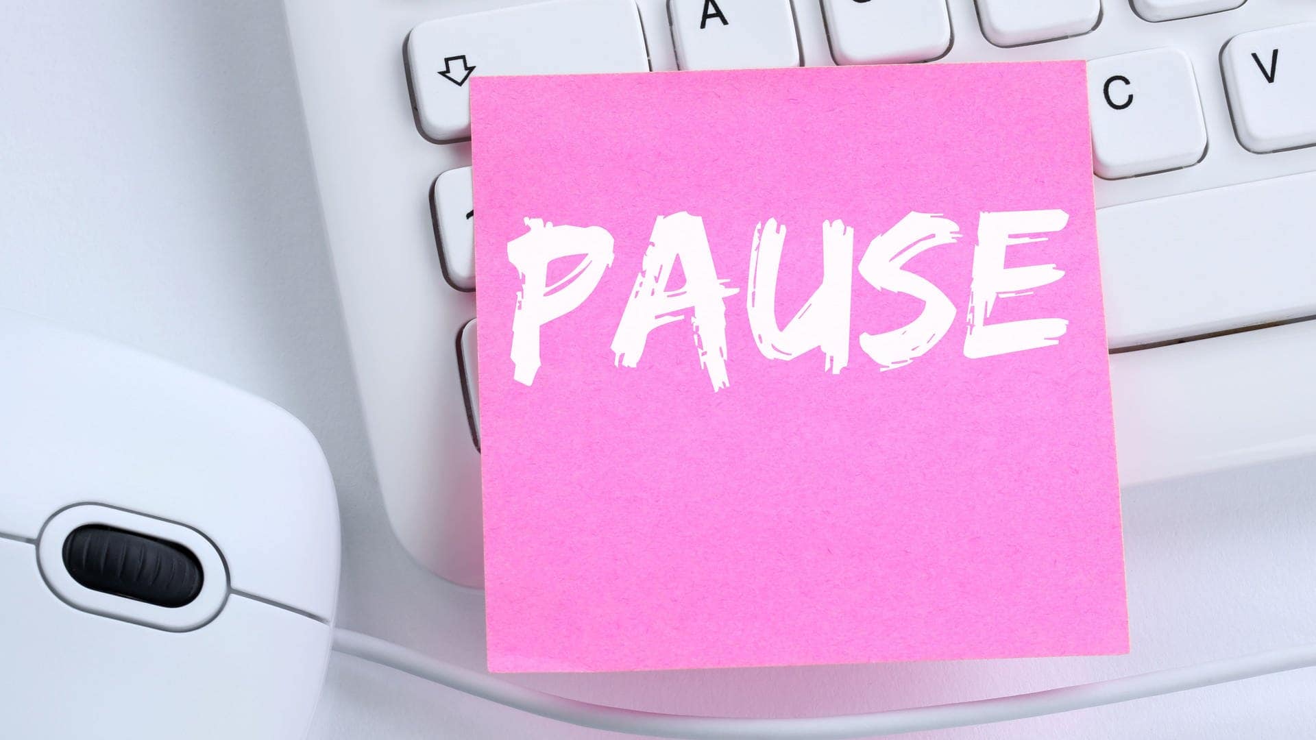Zettel mit dem Wort Pause liegt auf einem Schreibtisch, der nach Arbeit aussieht: auf einer Tastatur, neben einer Maus. (Foto: Adobe Stock, Markus Mainka)
