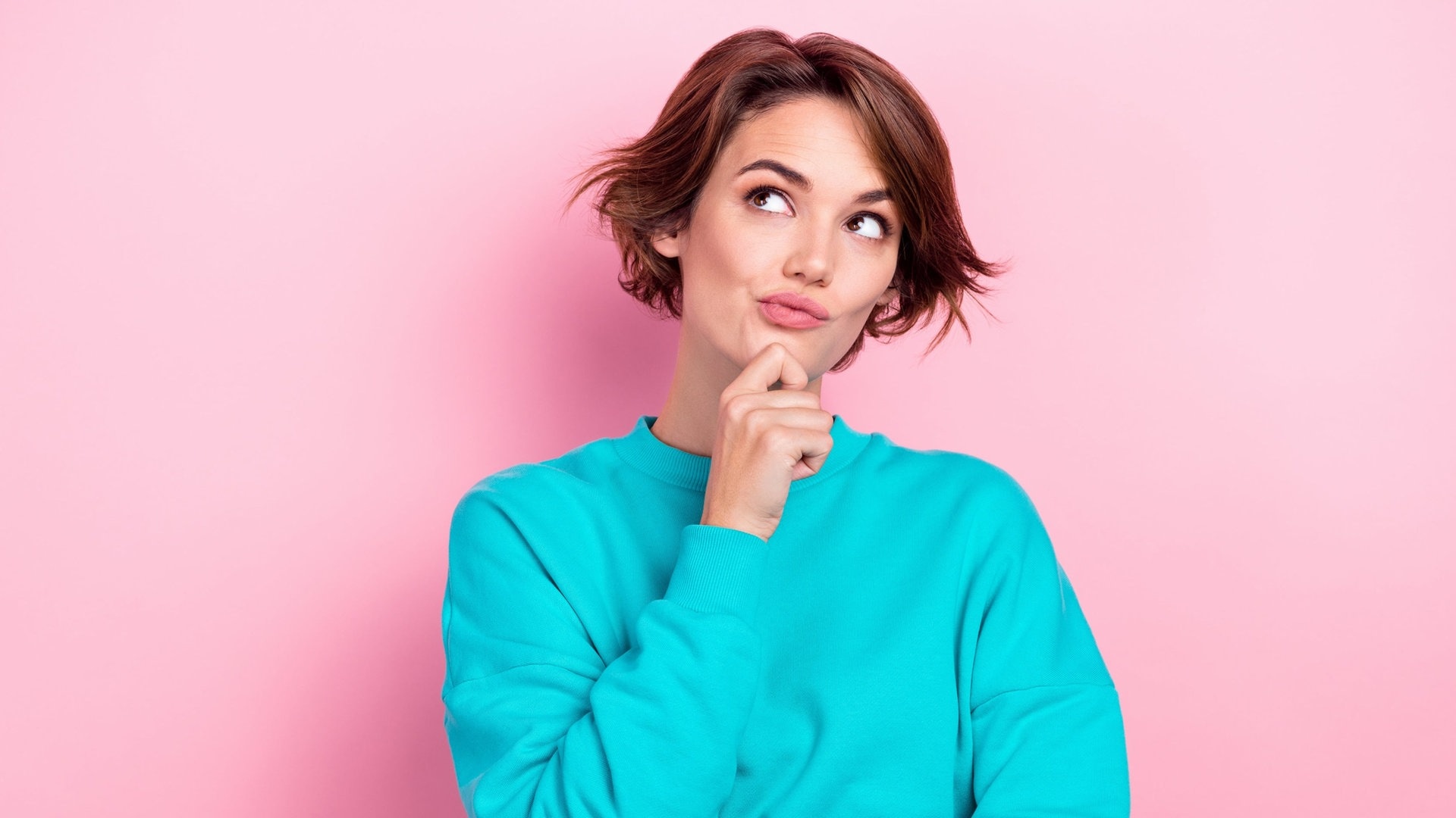 Junge Frau hält sich das Kinn und sieht nachdenklich aus – vielleicht grübelt sie über deutsche Rechtschreibung und Grammatik und sucht nach Eselsbrücken, um sie sich zu merken. (Foto: Adobe Stock, deagreez)