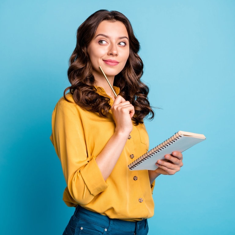 Junge Frau hält denkend einen Stift ans Kinn und einen Schreib-Block in der Hand. Vielleicht denkt sie gerade über Kommasetzung und Kommas in der deutschen Rechtschreibung nach. (Foto: Adobe Stock, https://www.swr3.de/aktuell/promi-news/jada-will-smith-getrennt-102.html)
