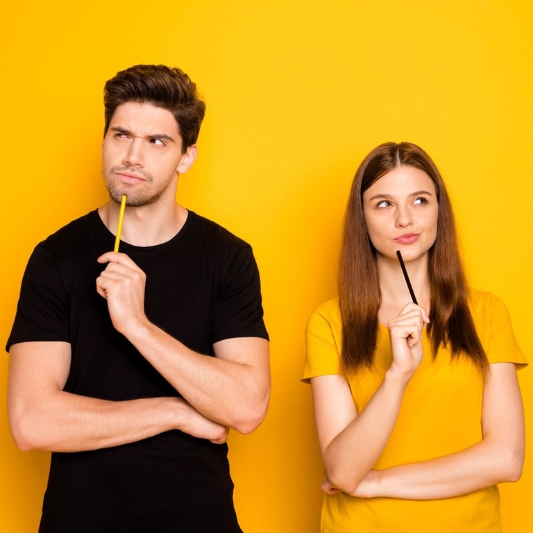Ein junger Mann und eine junge Frau machen ein grübelndes, nachdenkliches Gesicht. In der Hand halten sie Stifte, als würden gemeinsam das Plural-Quiz machen. (Foto: Adobe Stock, deagreez)