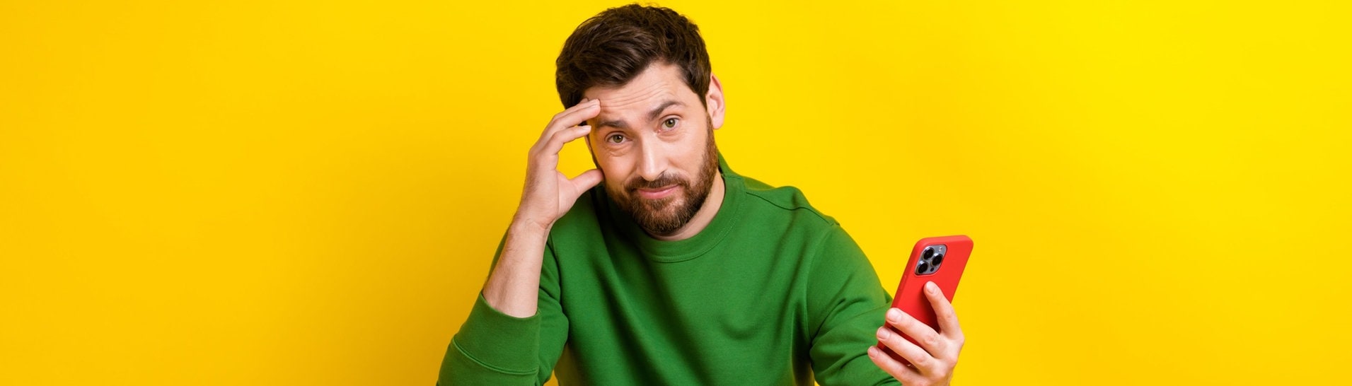 Junger Mann sitzt im Schneidersitz und mit dem Handy in der Hand auf einem Hocker. Er häkt denkend die Hand an den Kopf. Auf seinem Smartphone sieht er bestimmt gerade die überraschenden alternativen Schreibweisen laut Duden und wundert sich. (Foto: Adobe Stock, deagreez)
