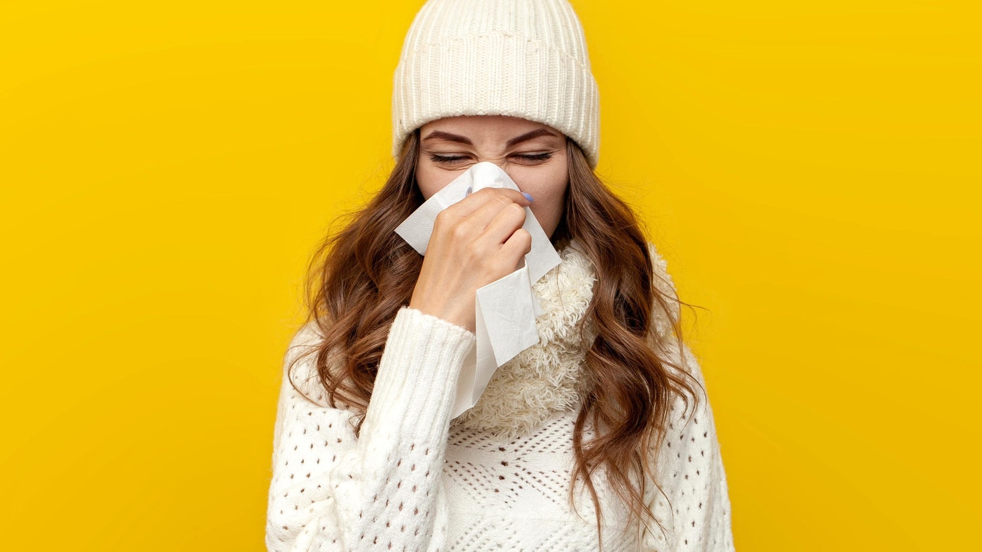 Junge Frau in Winter-Kleidung schnäuzt die Nase. Sie ist vermutlich krank und wird eine Krankschreibung für den Arbeitgeber brauchen oder sich zumindest krankmelden. (Foto: Adobe Stock, Богдан Маліцький)