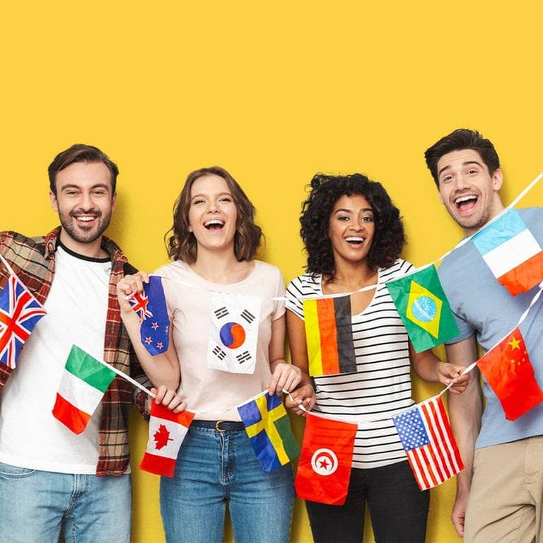 Vier Menschen mit unterschiedlichen Nationalitäten halten gemeinsam eine Girlande mit verschiedenen Flaggen. Sie lachen, vielleicht über die kuriosen Redewendungen aus den anderen Sprachen. (Foto: Adobe Stock, Drobot Dean)