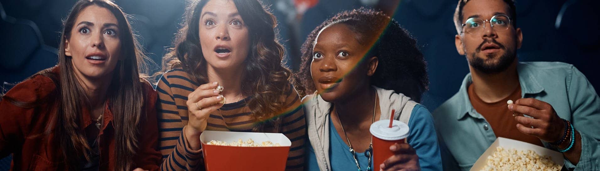 Darf man Snacks mit ins Kino nehmen? Eine Gruppe von Menschen sitzt mit Snacks im Kino schaut gespannt (Foto: Adobe Stock, Drazen)