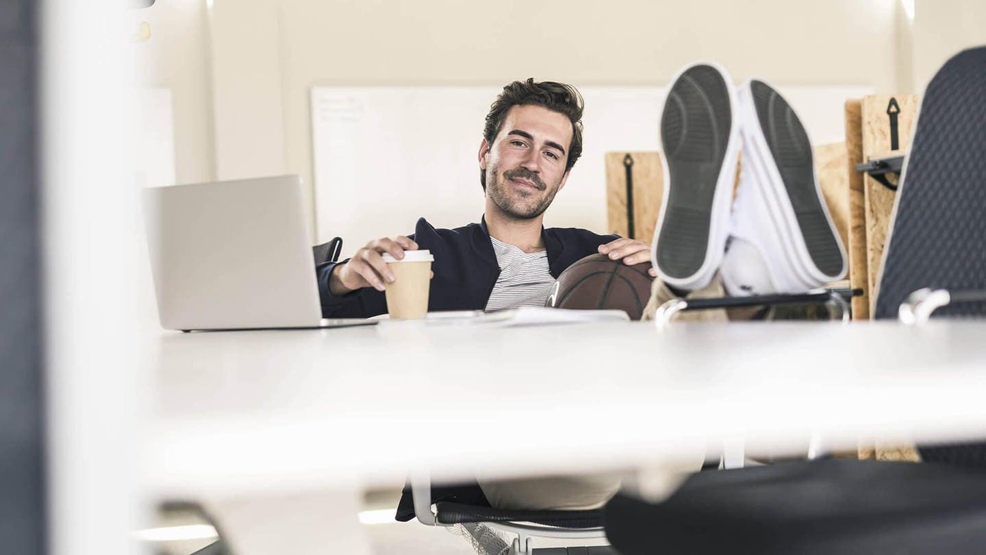 Mann im Büro mit Füßen auf dem Tisch und einem Becher Kaffee (Foto: imago/Westend61)