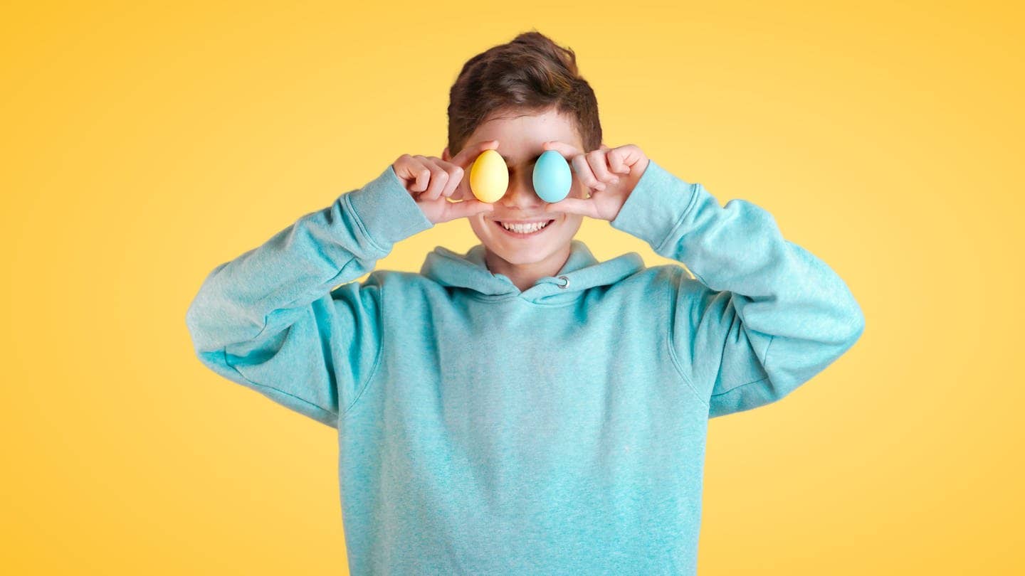 Junge hält zwei bunte Eier vor seine Augen. (Foto: Adobe Stock)
