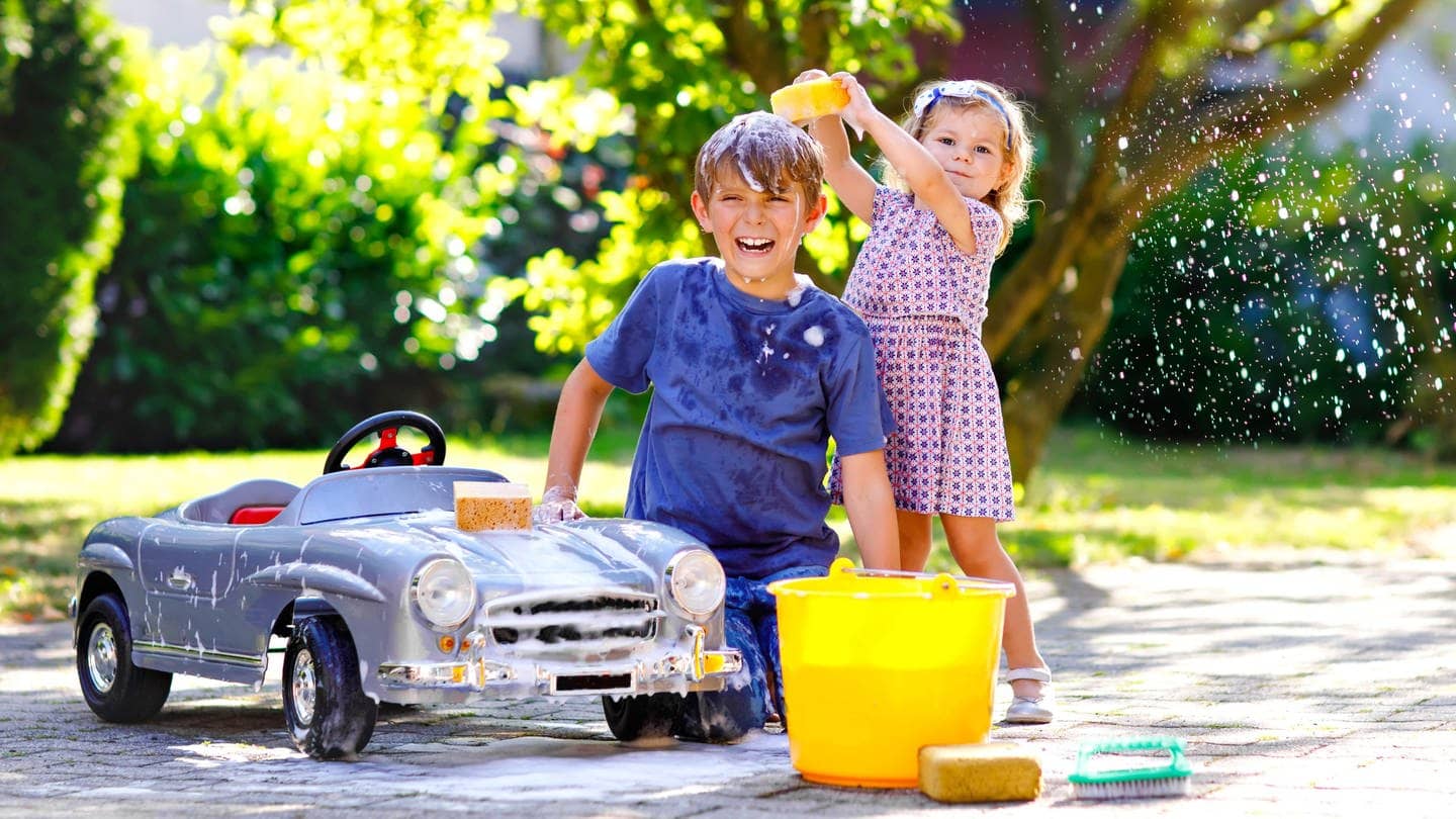Junge und Mädchen beschäftigen sich an einem kleinen Auto mit der Autoreinigung. Symbolbild für Hausmittel, um das Auto nach dem Saharastaub zu waschen.