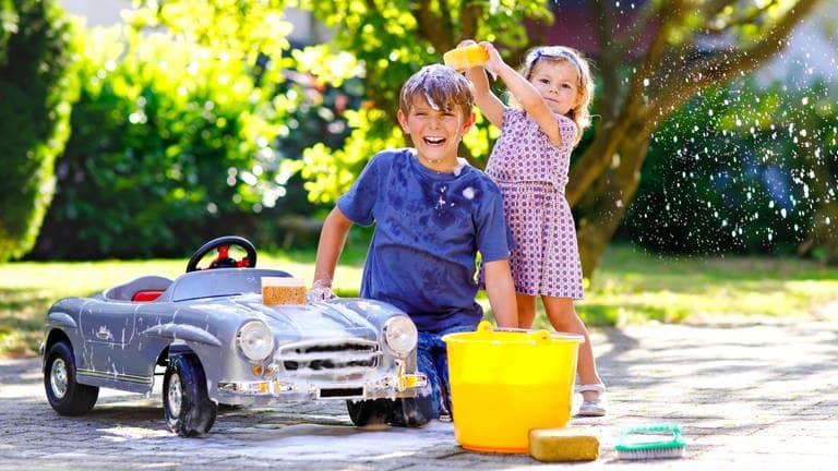 Junge und Mädchen beschäftigen sich an einem kleinen Auto mit der Autoreinigung. Symbolbild für Hausmittel, um das Auto nach dem Saharastaub zu waschen. (Foto: Adobe Stock, Irina Schmidt)