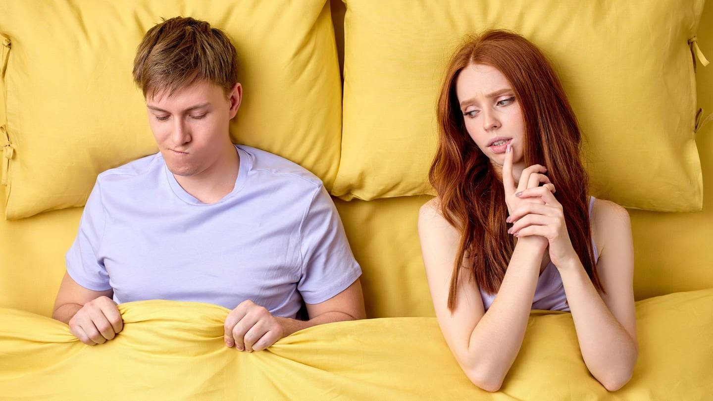 Junges Paar liegt im Bett. Sie schaut skeptisch zu ihm rüber, er ist verunsichert, weil er keine Lust hat auf Sex.
