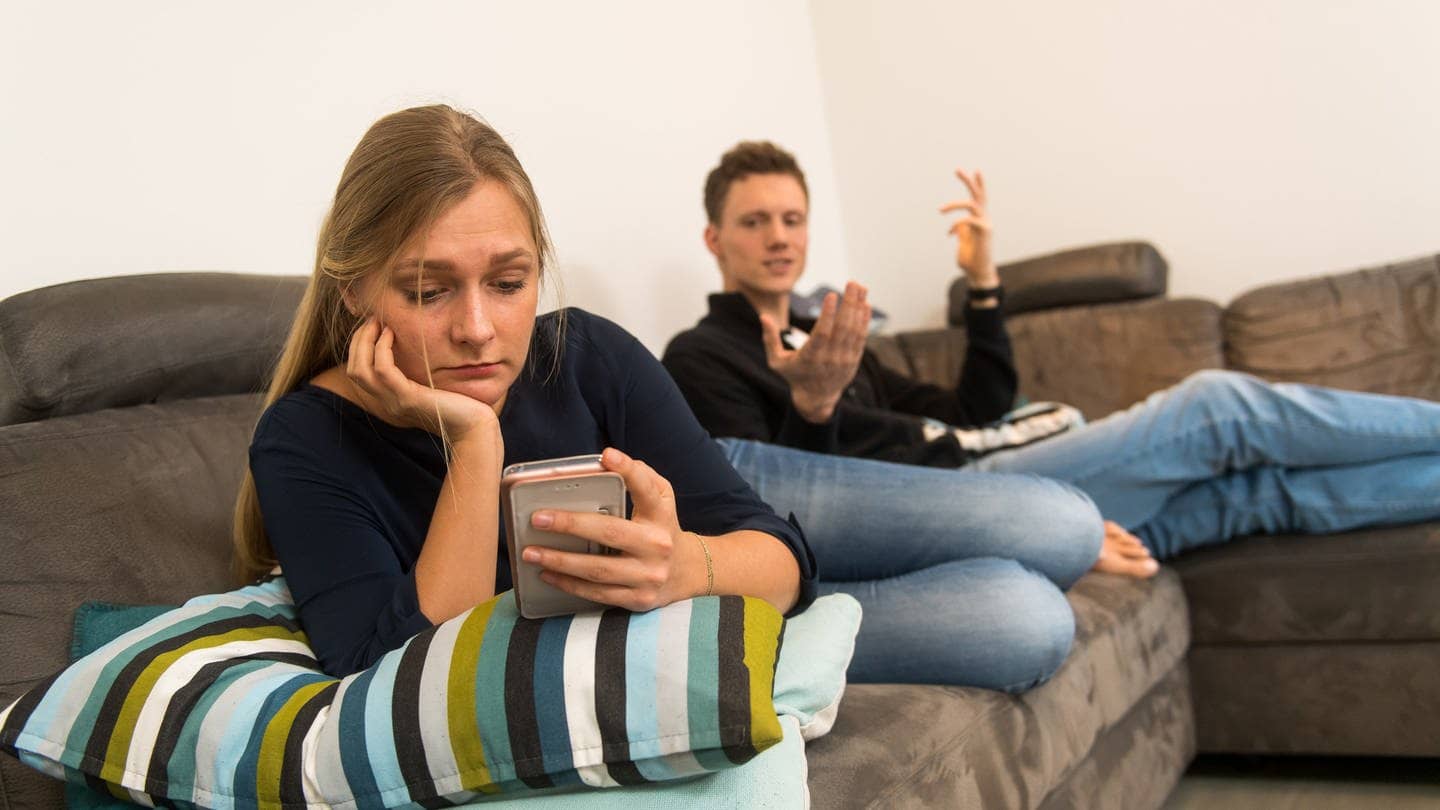 Ein Paar streitet sich auf einem Sofa, weil sie ihm zu oft am Smartphone ist.