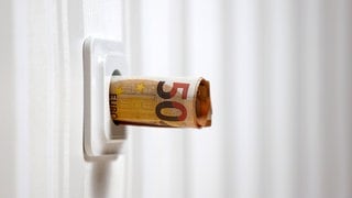 Symbolbild für die Energiekrise: Zusammengerollte Geldscheine ragen aus einer Steckdose. 