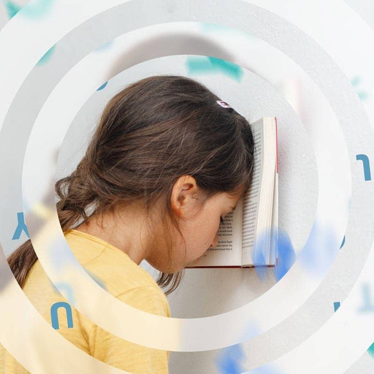 Ein Mädchen im Grundschulalter lehnt mit dem Kopf an einem Buch an der Wand. Im Hintergrund schwirren Buchstaben um sie herum. (Foto: Adobe Stock, Julia)