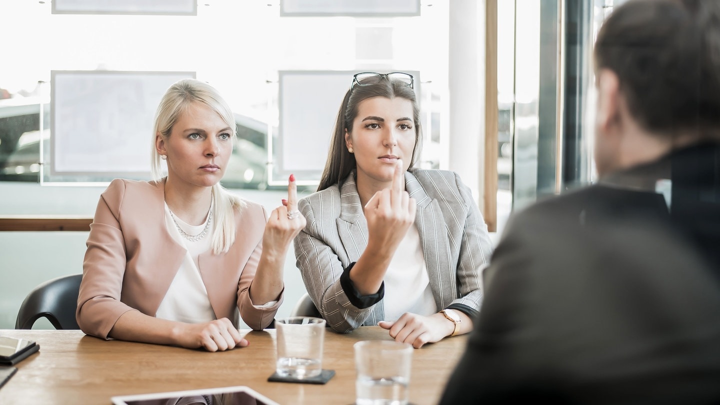 Zwei Frauen zeigen ihrem Chef den Mittelfinger