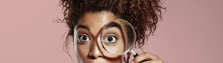 Überraschte Frau schaut durch eine Lupe.