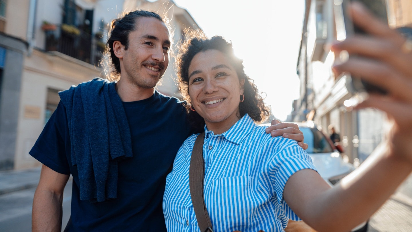 Zwei Touristen nehmen gemeinsam ein Foto mit einer Handykamera bei einer Städtereise auf.