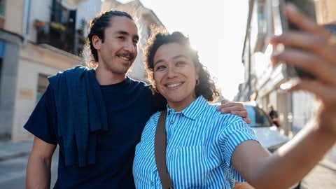 Zwei Touristen nehmen gemeinsam ein Foto mit einer Handykamera bei einer Städtereise auf.