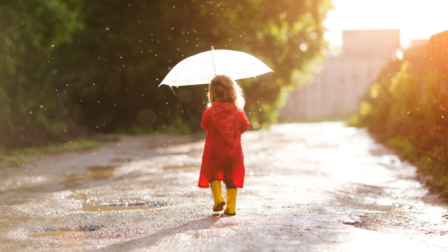 Ein Kind läuft mit Schirm und Gummistiefeln durch den Regen.