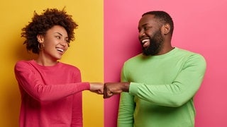 Junges Paar steht lachend vor einer durch zwei Farben getrennten Wand. Sie schlagen sie ab und sehen glücklich aus mit der Beziehung. (Foto: Adobe Stock, Wayhome Studio) Junges Paar steht lachend vor einer durch zwei Farben getrennten Wand. Sie schlagen sie ab und sehen glücklich aus mit der Beziehung.
