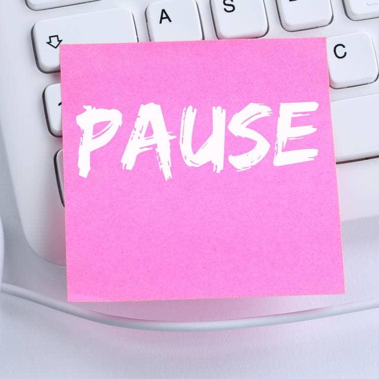 Zettel mit dem Wort Pause liegt auf einem Schreibtisch, der nach Arbeit aussieht: auf einer Tastatur, neben einer Maus.