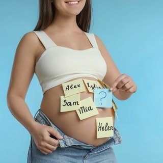Auf den Bauch einer schwangeren Frau sind bunte Zettel mit verschiedenen Vornamen geklebt.