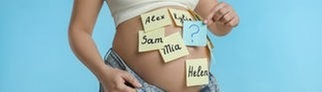Auf den Bauch einer schwangeren Frau sind bunte Zettel mit verschiedenen Vornamen geklebt.