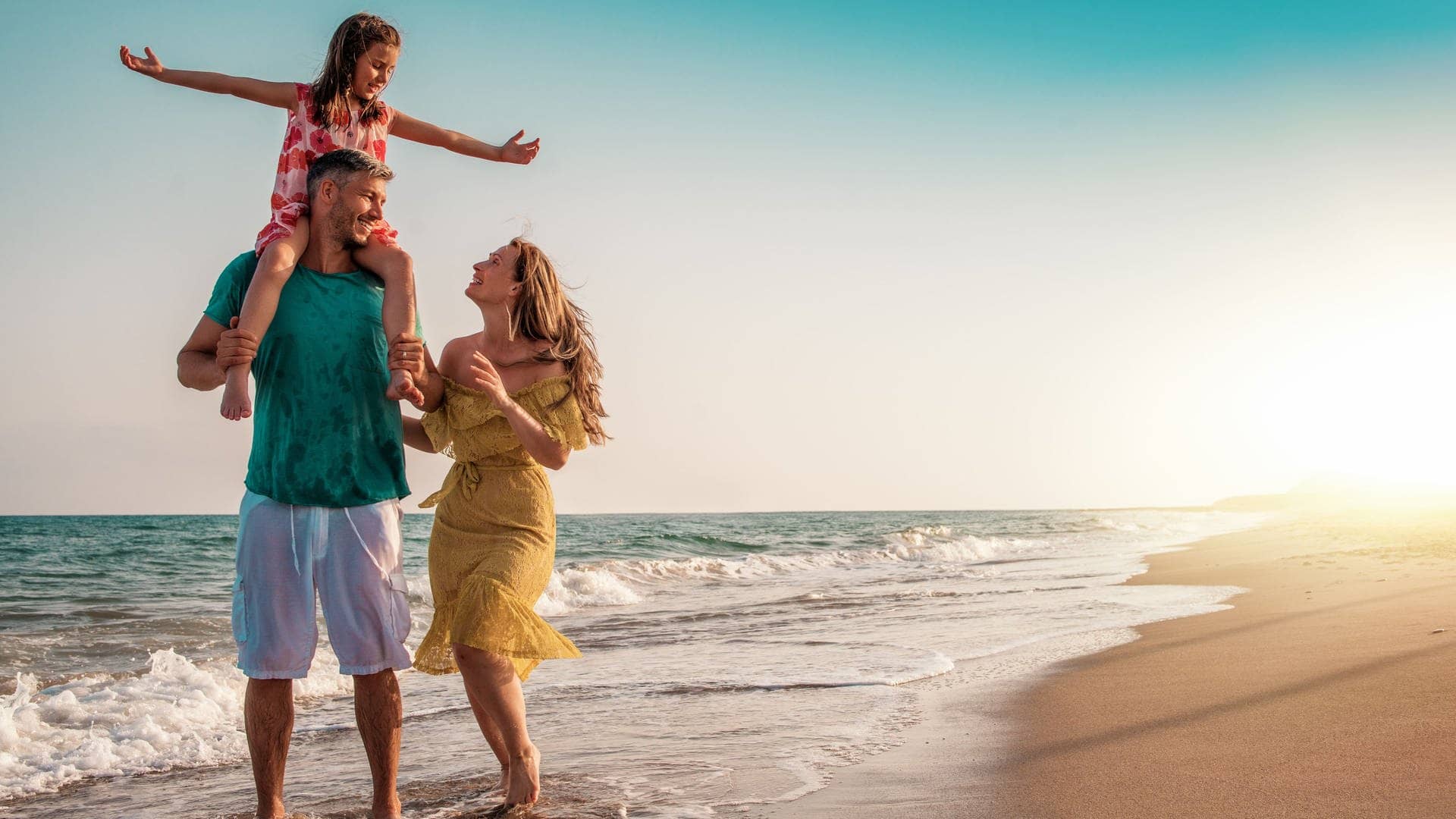 Eine junge Familie spaziert am Strand. Mann, Frau und ein Kind auf den Schultern des Vaters im Urlaub. Es drohen keine Konsequenzen und es ist keine Arbeitsverweigerung, wenn sie sich von hier aus nicht zurück zur Arbeit holen lassen. (Foto: Adobe Stock, detailblick-foto)