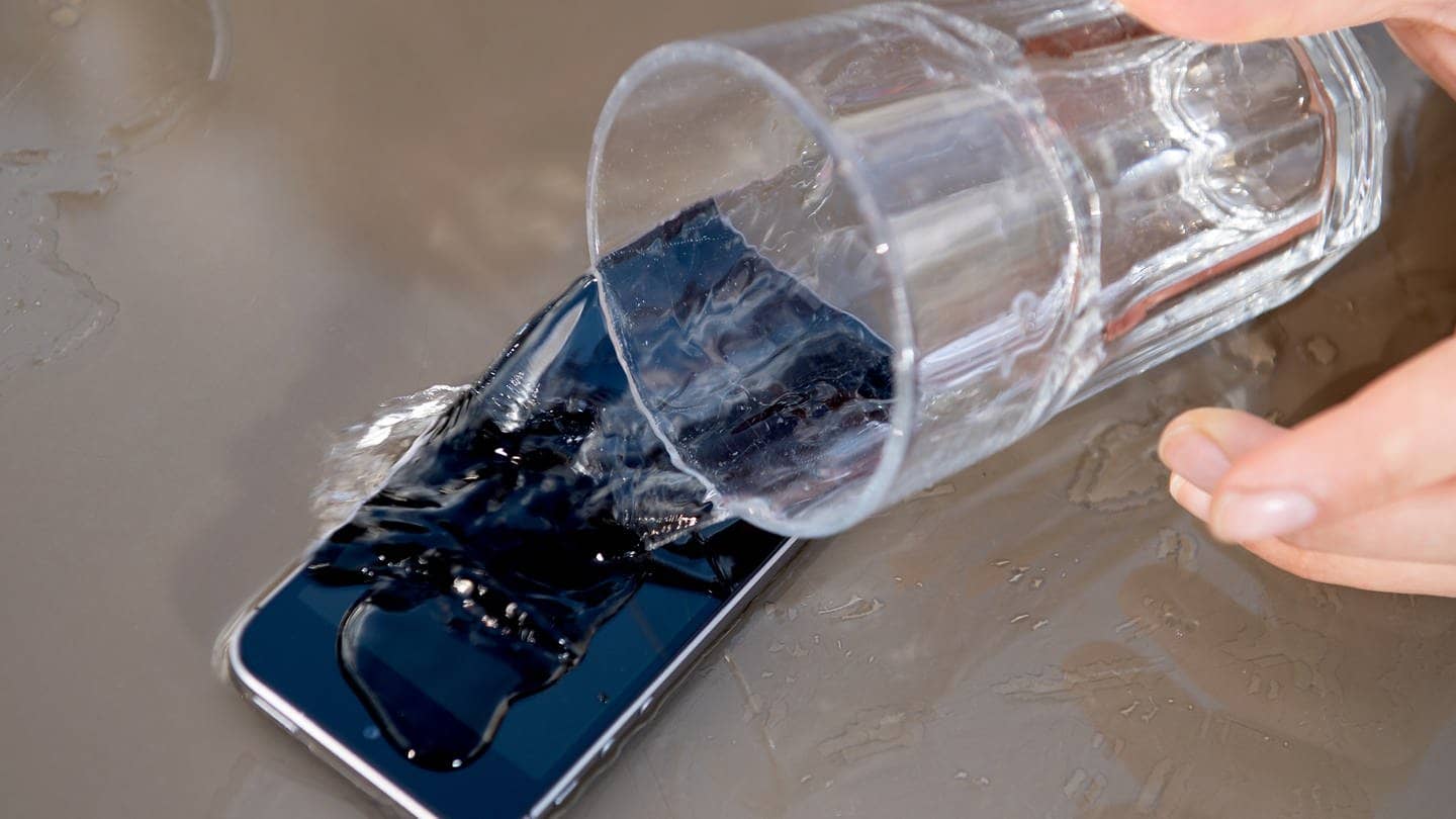 Ein Glas Wasser wird über ein Handy geschüttet. (Foto: picture-alliance / Reportdienste, picture alliance / dpa Themendienst | Franziska Gabbert)