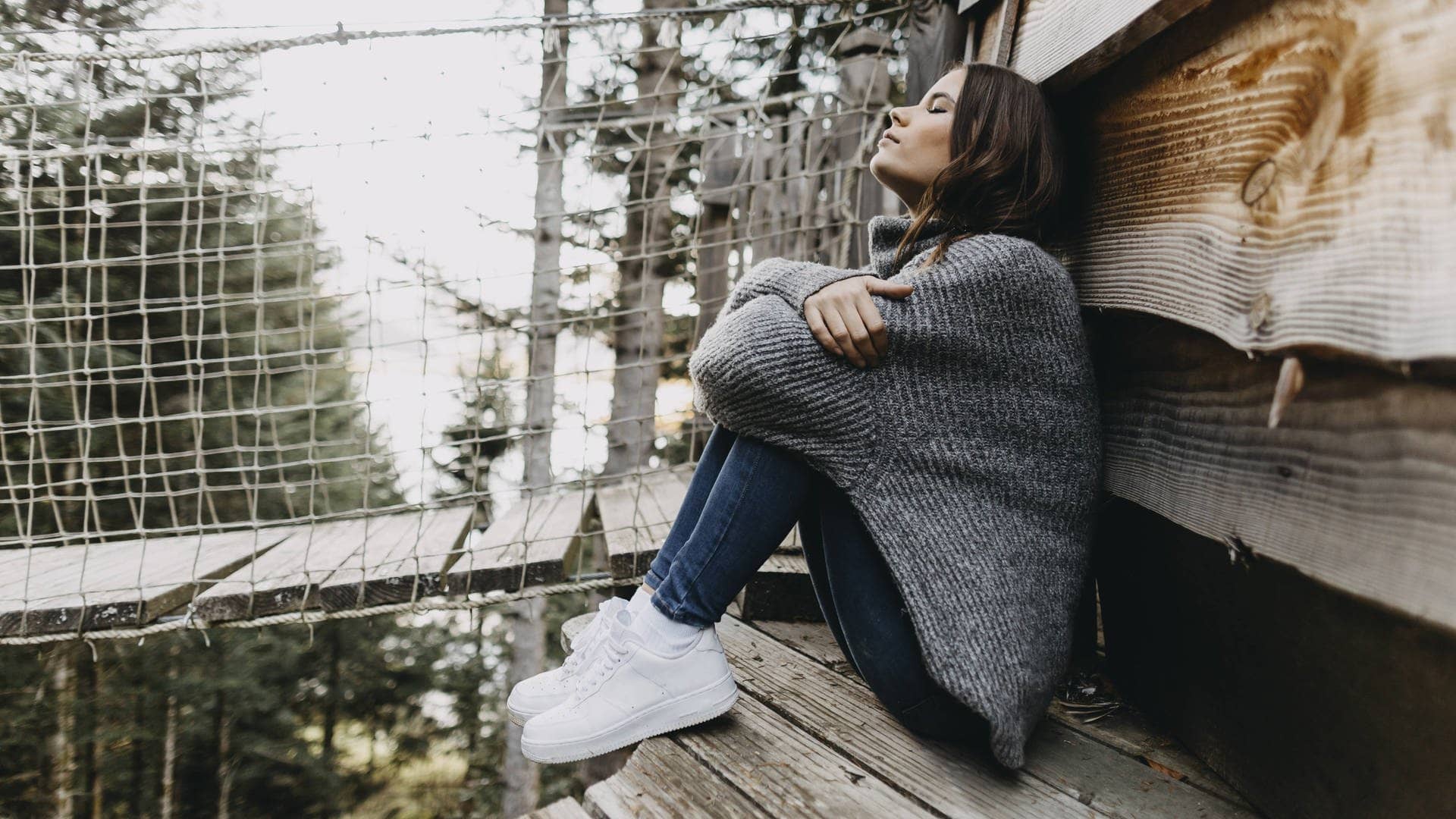 Warum der November ein toller Monat ist – Grund 1: Entschleunigung. Symbolbild von einer jungen Frau, die im Wald angelehnt an eine Holzhütte sitzt. (Foto: IMAGO, IMAGO / Westend61)