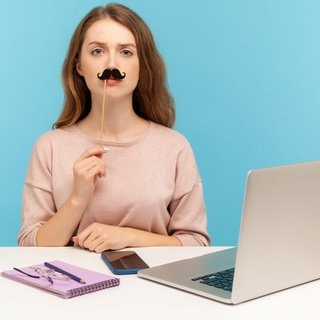 Tipps, um einen Fake Shop zu erkennen. Frau mit Fake-Bart vorm Laptop
