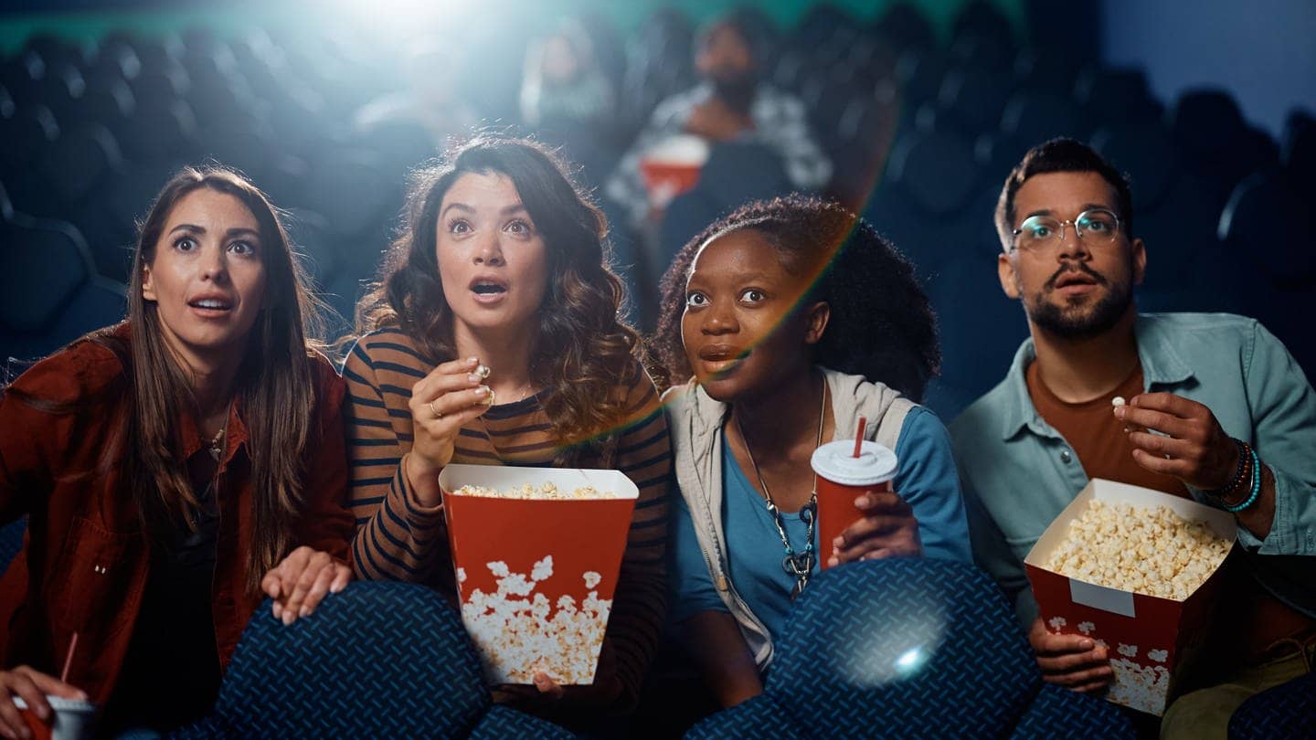 Darf man Snacks mit ins Kino nehmen? Eine Gruppe von Menschen sitzt mit Snacks im Kino schaut gespannt