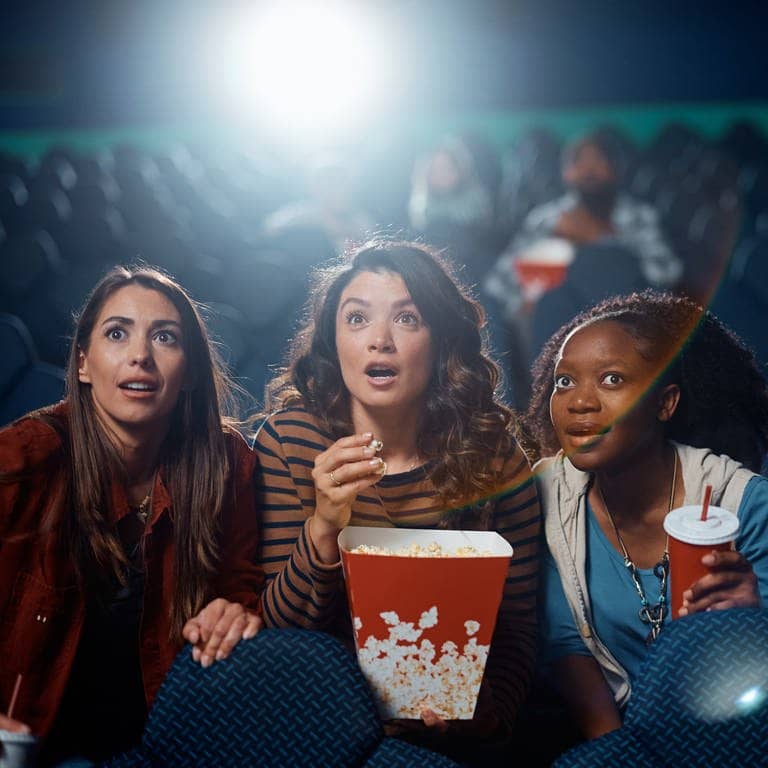 Darf man Snacks mit ins Kino nehmen? Eine Gruppe von Menschen sitzt mit Snacks im Kino schaut gespannt