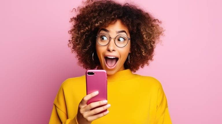 Junge Frau rätselt an ihrem rosafarbenen Smartphone über Abkürzungen aus dem Internet und lacht.