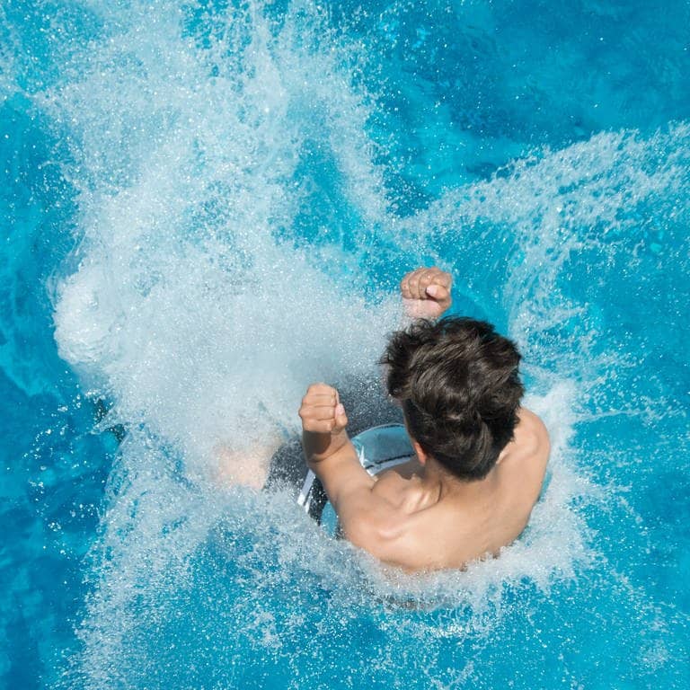 Hitze im Sommer: Ein Mann springt von einem Sprungturm in ein Schwimmbecken.
