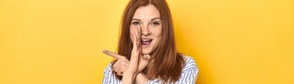 Junge Frau hält ihre Hand seitlich an den Mund, um eine unpopuläre Meinung zu verraten